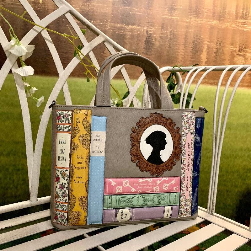Two bags, navy and grey, sat on the a bench. Each decorated with Jane Austen books and silhouette