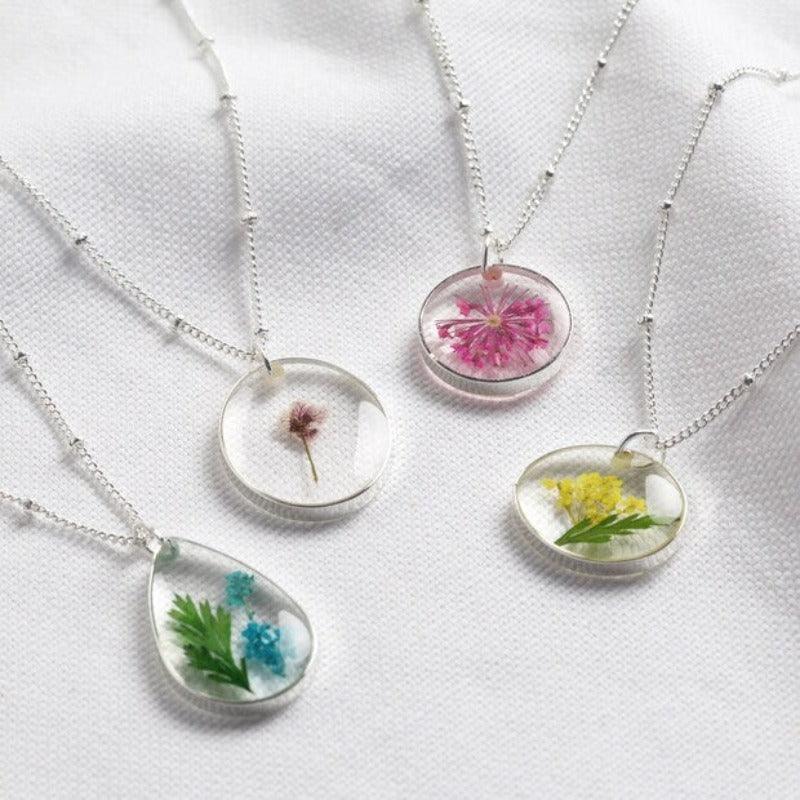 Four beautiful flower pendent necklaces laid out. Each flower is pressed and encapsulated in clear resin and hung on a silver chain. 