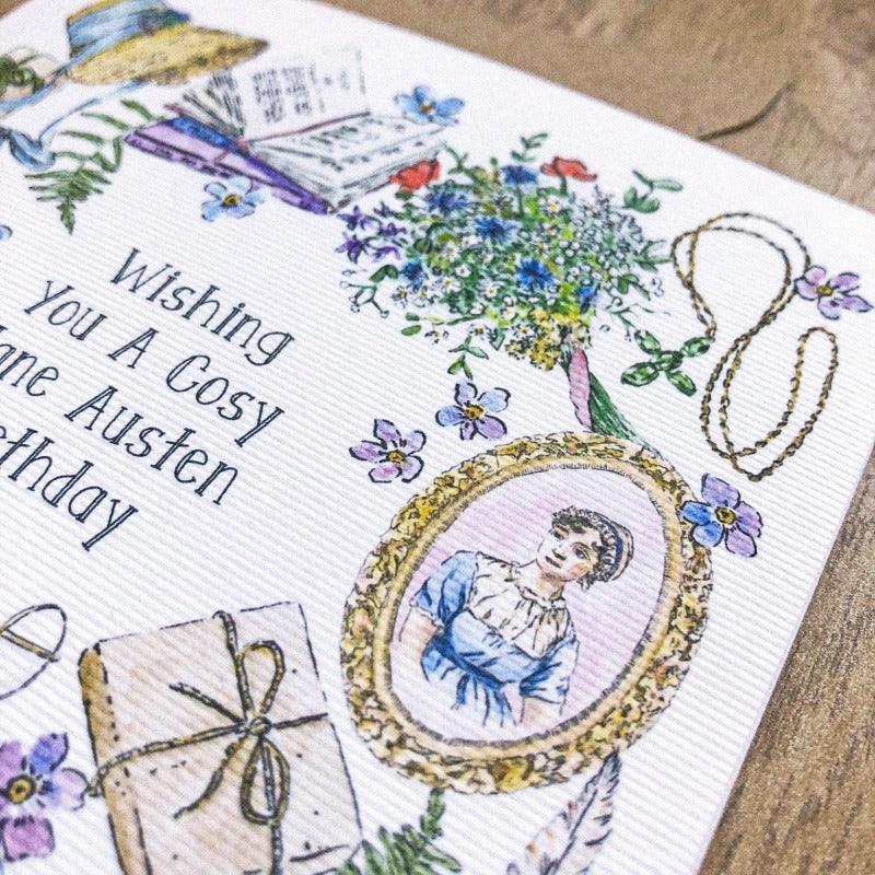 A close up shot of the "wishing you a cosy jane austen birthday" card. Showing the delicate ribbing in the card stock and the detail to the hand illustrated design. 