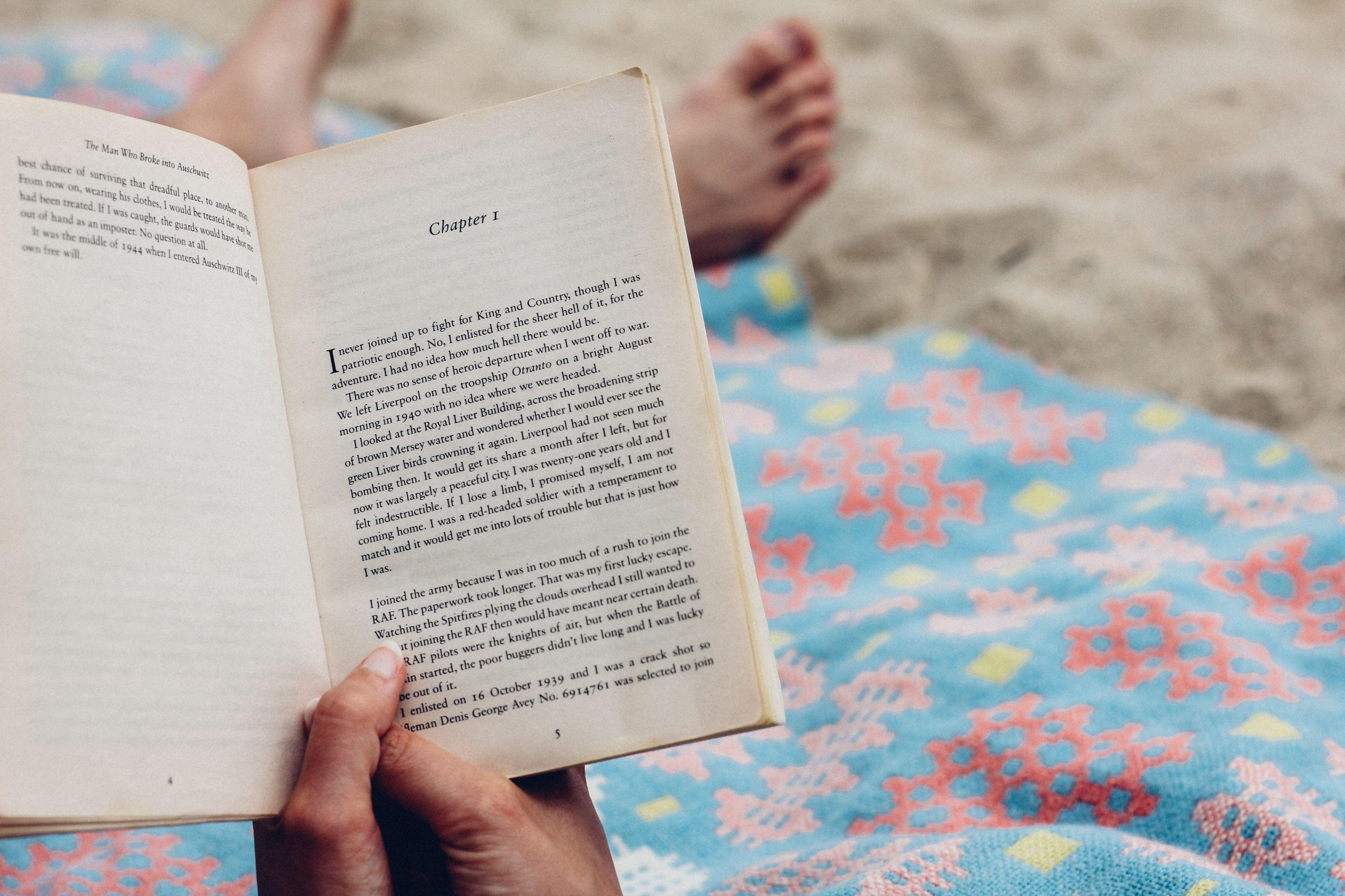 Person reading book on beach, with beach towel 